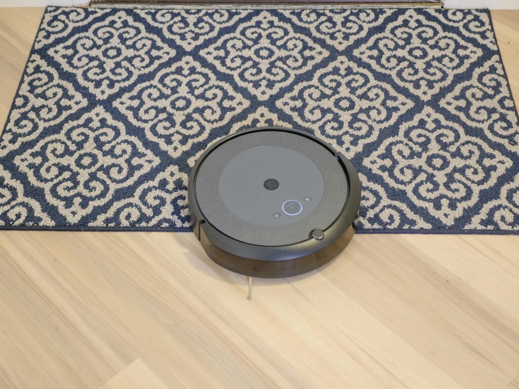 A modern robotic vacuum cleaning a stylish patterned carpet on a wooden floor.
